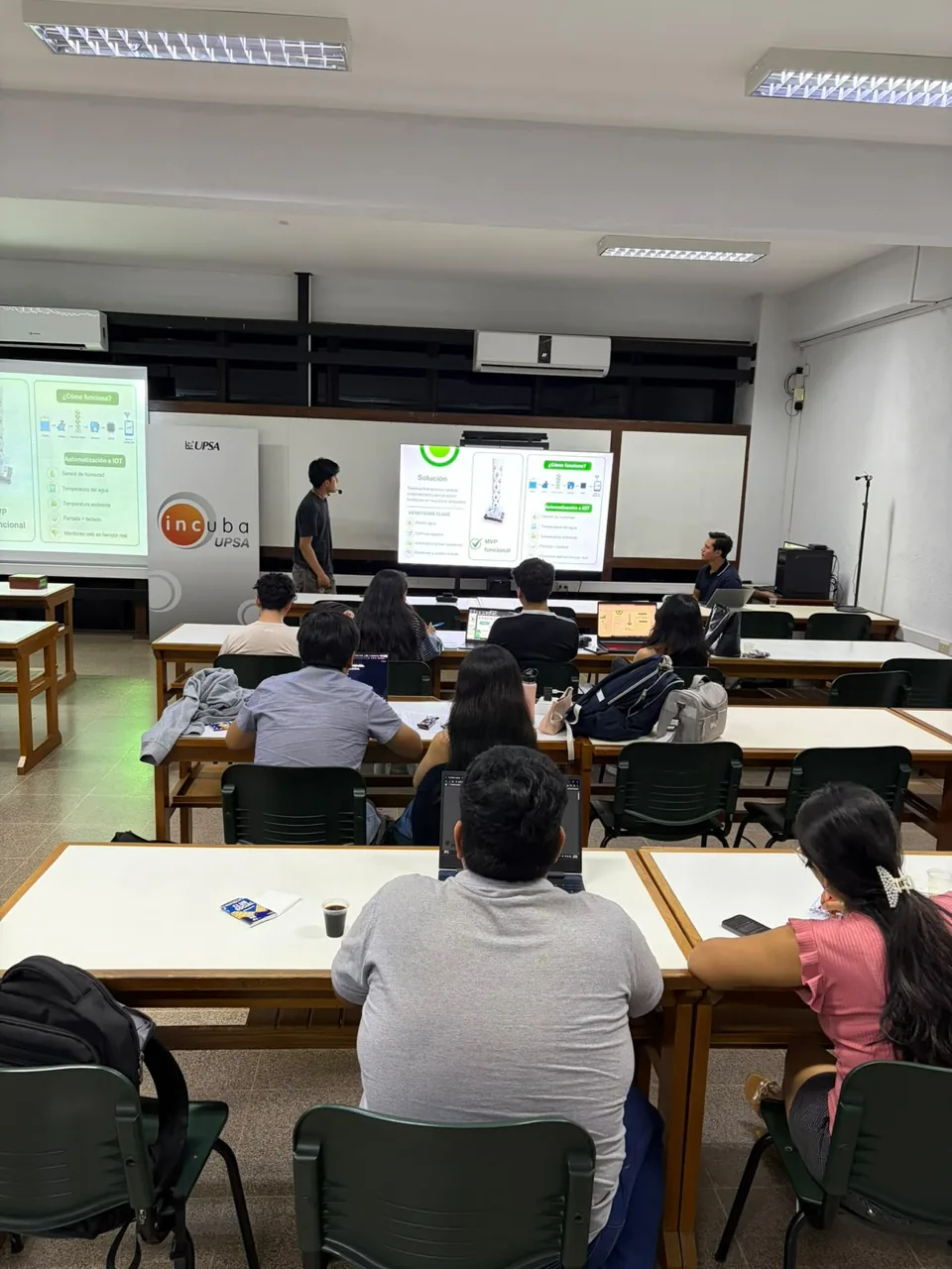 Participantes en un taller, con una presentación y equipos de trabajo.